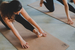 Tapete Yoga em cortiça - Alongamento da zona posterior da perna em contexto de aula - foto visão ampla com duas yoginis em plano
